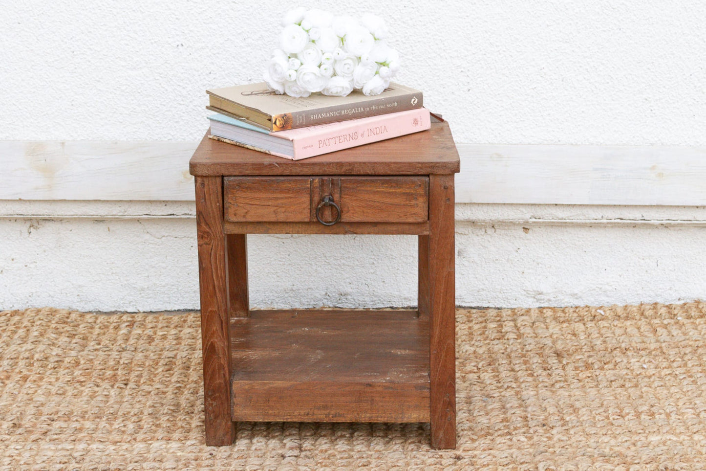 Wooden side table with books and flowers on a textured rug