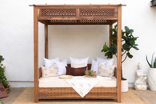 Wooden canopy bed with white bedding and decorative pillows in a room with plants.