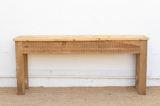 Wooden console table with wicker drawer front against a white wall.