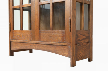 A close-up of a wooden cabinet or bookcase with glass-paneled upper doors and a curved lower drawer front, shown against a plain white background.