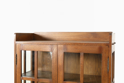 A close-up of a wooden cabinet or changing table with glass-front doors and a warm medium-brown wood finish, shown against a plain white background.