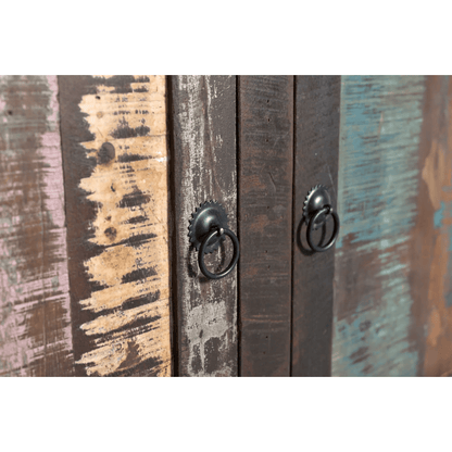 Close-up of rustic wooden cabinet doors with distressed paint in brown, beige, and teal tones, featuring two black metal ring pulls with decorative caps.