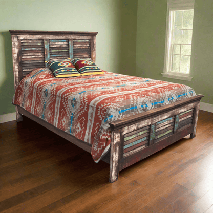 A rustic reclaimed wood bed frame with a slatted headboard and footboard, styled with a southwestern patterned red, blue, and white quilt and colorful pillows, set in a room with green walls and hardwood floors.