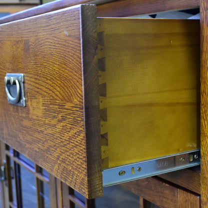 Close-up of a wooden drawer pulled open, showing the wood grain exterior, brass-toned interior, and metal drawer slide hardware.