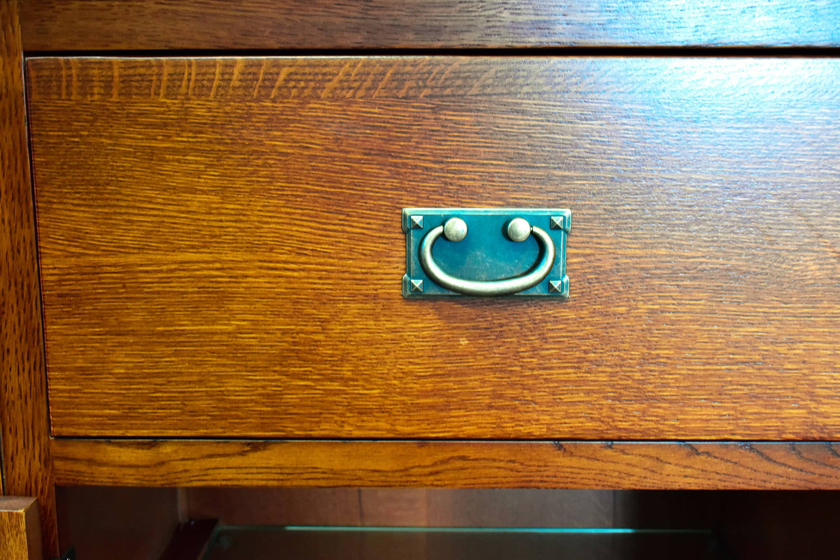 Close-up of a medium brown wooden drawer front with a square brass pull handle mounted in the center.