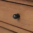 A close-up of a round black metal drawer knob mounted on a warm brown wooden drawer front.
