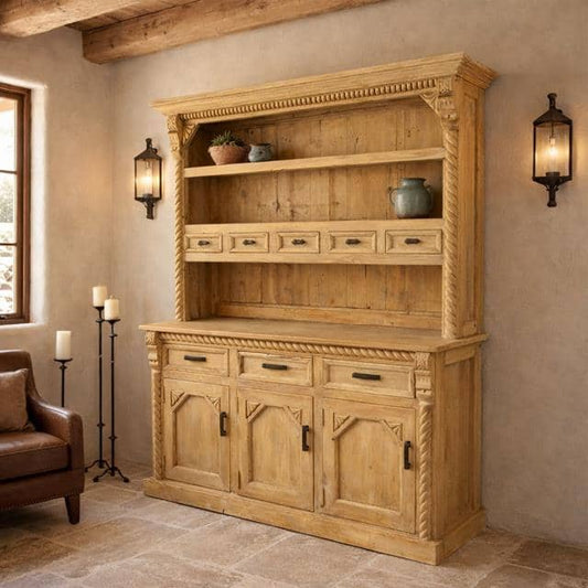 A large rustic wooden hutch or buffet cabinet with carved details, rope-textured trim, open shelves, and three lower cabinet doors, shown in a styled room with wall sconces, candles, and a chair.