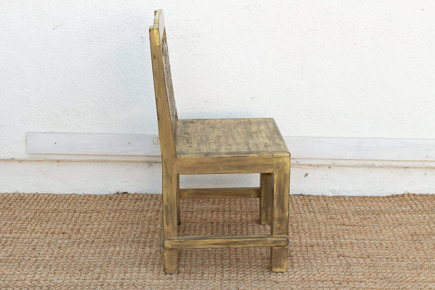 Wooden chair with a woven backrest on a textured floor against a white wall