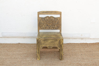 Wooden chair with intricate carvings on a textured floor and white wall background