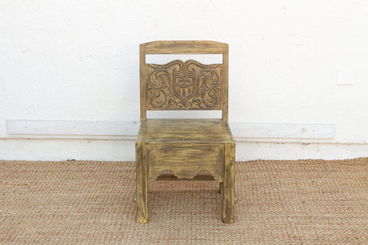 Wooden chair with intricate carvings on a textured floor and white wall background