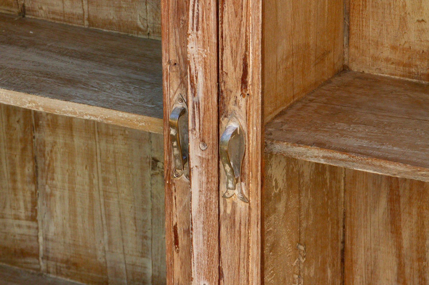 Close-up of rustic wooden cabinet doors with weathered metal handles and matching wooden shelves.