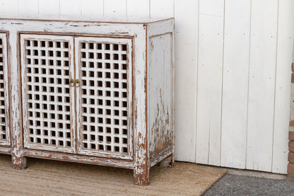 Vintage-style wooden cabinet with lattice doors against a white wall.