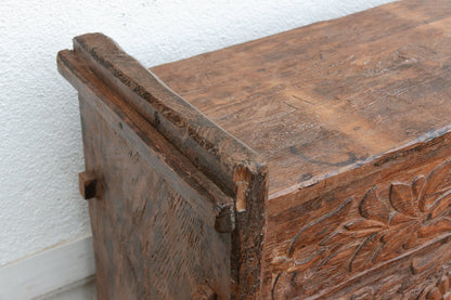 Close-up of an old wooden chest with carvings on a white wall.