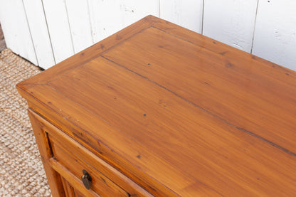 Wooden dresser with a single drawer against a white paneled wall.