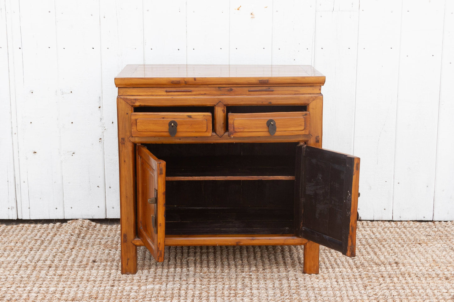Wooden sideboard with open doors against a white paneled wall.