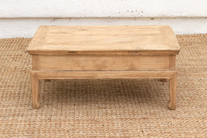 Wooden coffee table on a textured rug with a white wall background