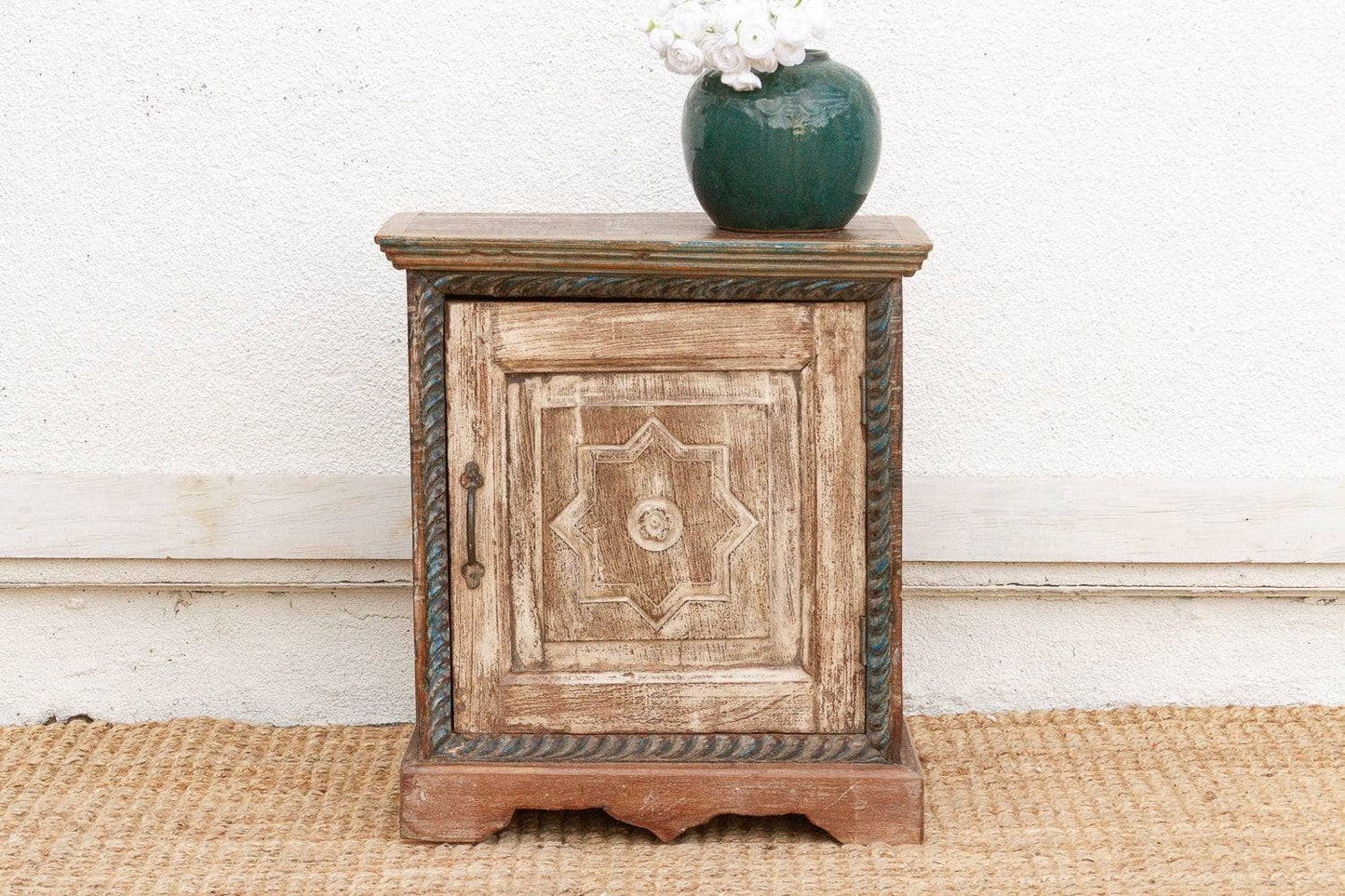 Wooden side table with decorative design on a white wall background