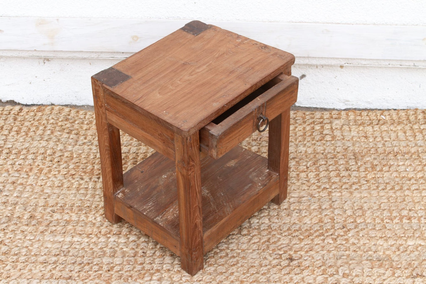 Wooden side table with a drawer on a textured floor.