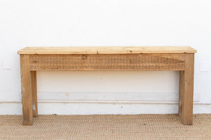 Wooden console table with wicker drawer front against a white wall.