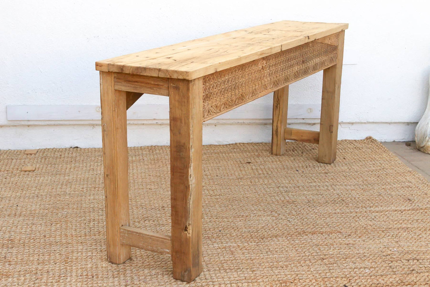 Wooden bench on a textured floor with a white wall background