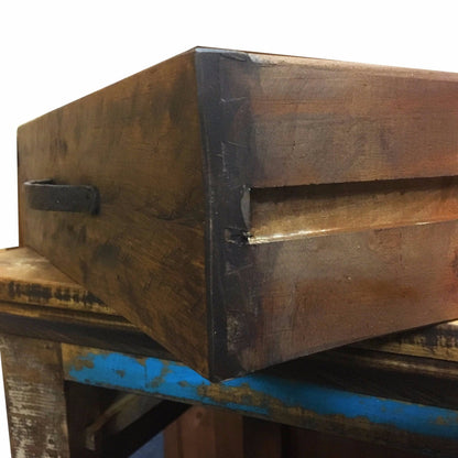 A rustic dark brown wooden box with a black metal handle, resting on a weathered blue and wood table against a white background.