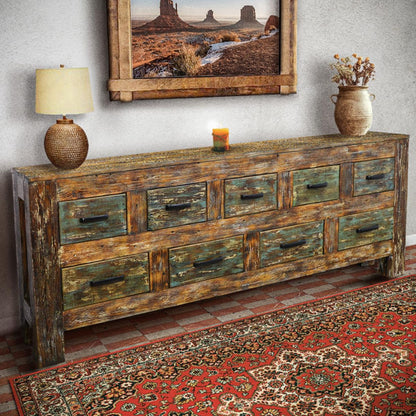 Wooden dresser with rustic finish in a room with a lamp, vase, and framed picture on the wall.